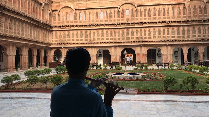 Laxmi Niwas Palace Bikaner luxury heritage hotel photo of lone musican surrounded by sunlit sandstone carved walls